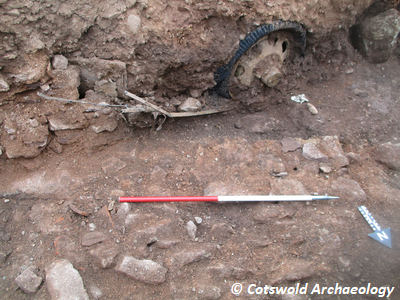 Rough stone wall 102, bonded with brown sandy mortar. Images also shows artefactual material (automotive components, in this case a tyre) typical of mid-20th century activity. Copyright: Cotswold Archaeology